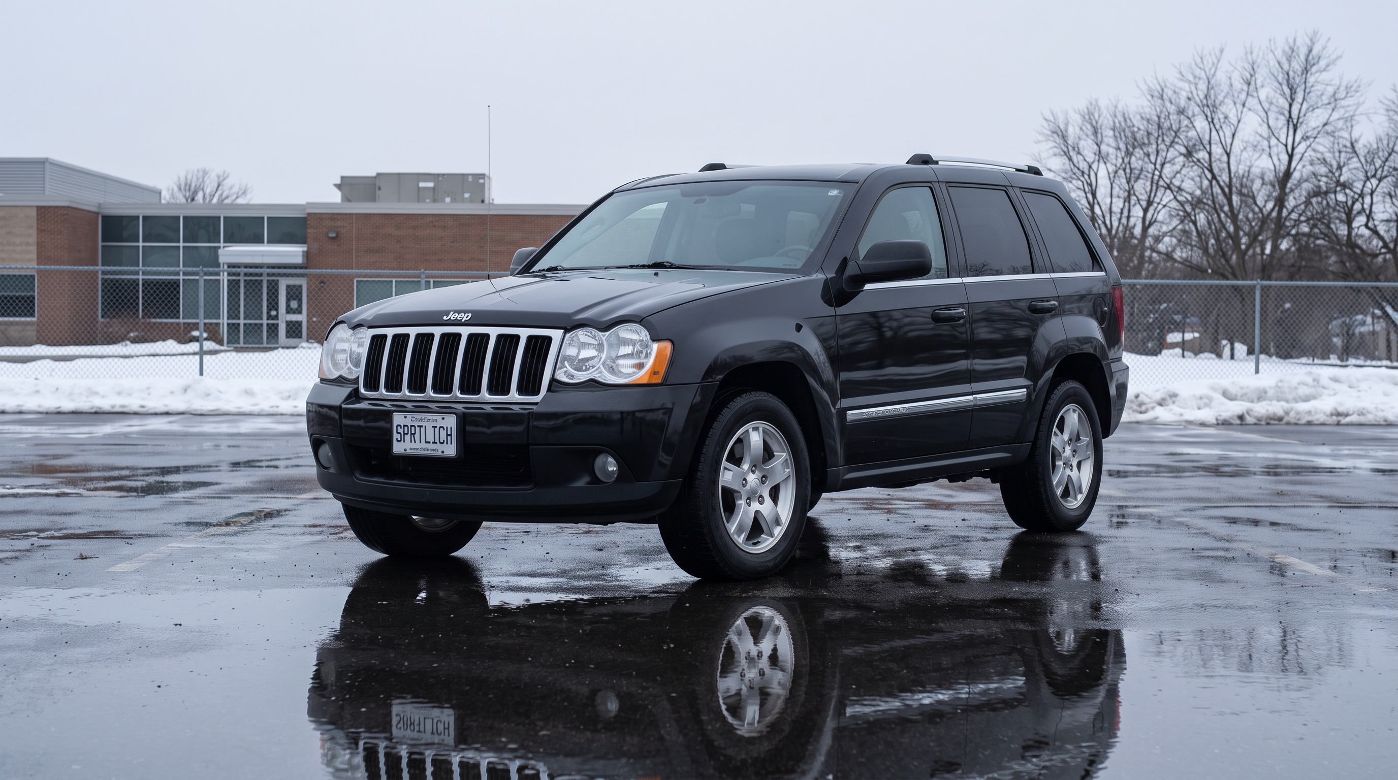 A black WK-generation Jeep Grand Cherokee alone on a wet, empty car park in winter