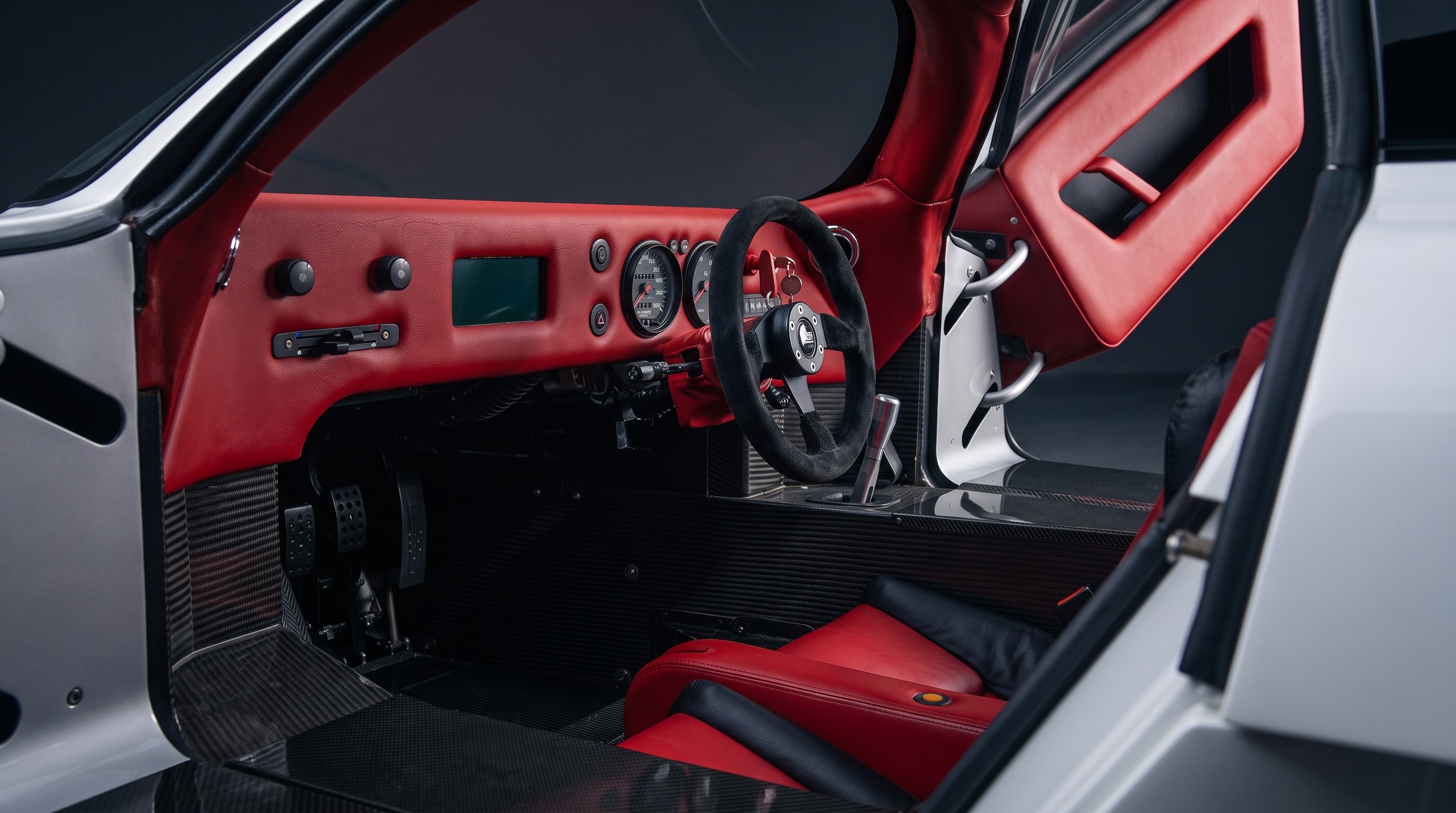 The Lotec C1000 cockpit with red leather dashboard, exposed carbon tub, small steering wheel and metal gear lever